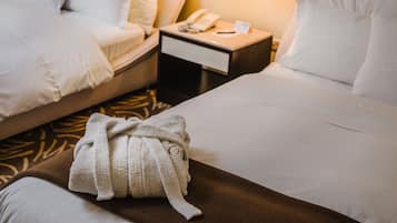 Habitación de hotel con dos camas, una mesita de noche con un teléfono y una lámpara, y una bata sobre la cama.
