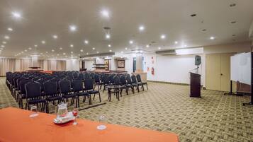 Un salón de conferencias con filas de sillas, un atril y una mesa con una jofaina y vasos.