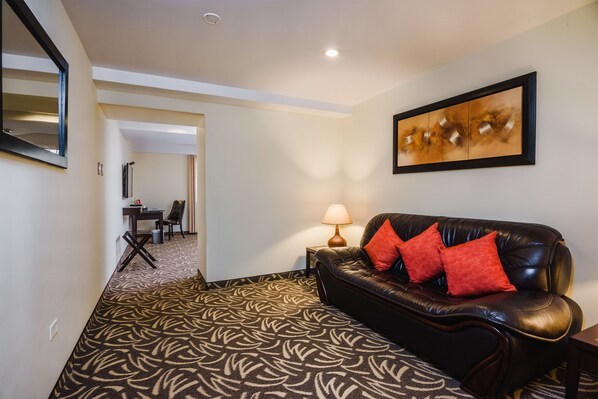 Un salon moderne avec un tapis à motifs, un canapé en cuir avec des coussins rouges, une table d’appoint avec une lampe et un tableau abstrait encadré accroché au mur.
