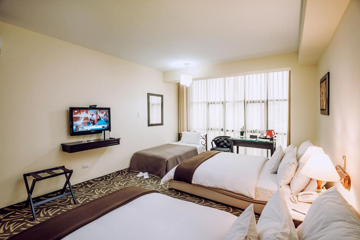 A hotel room with two beds, a television, a desk, and a window with curtains.