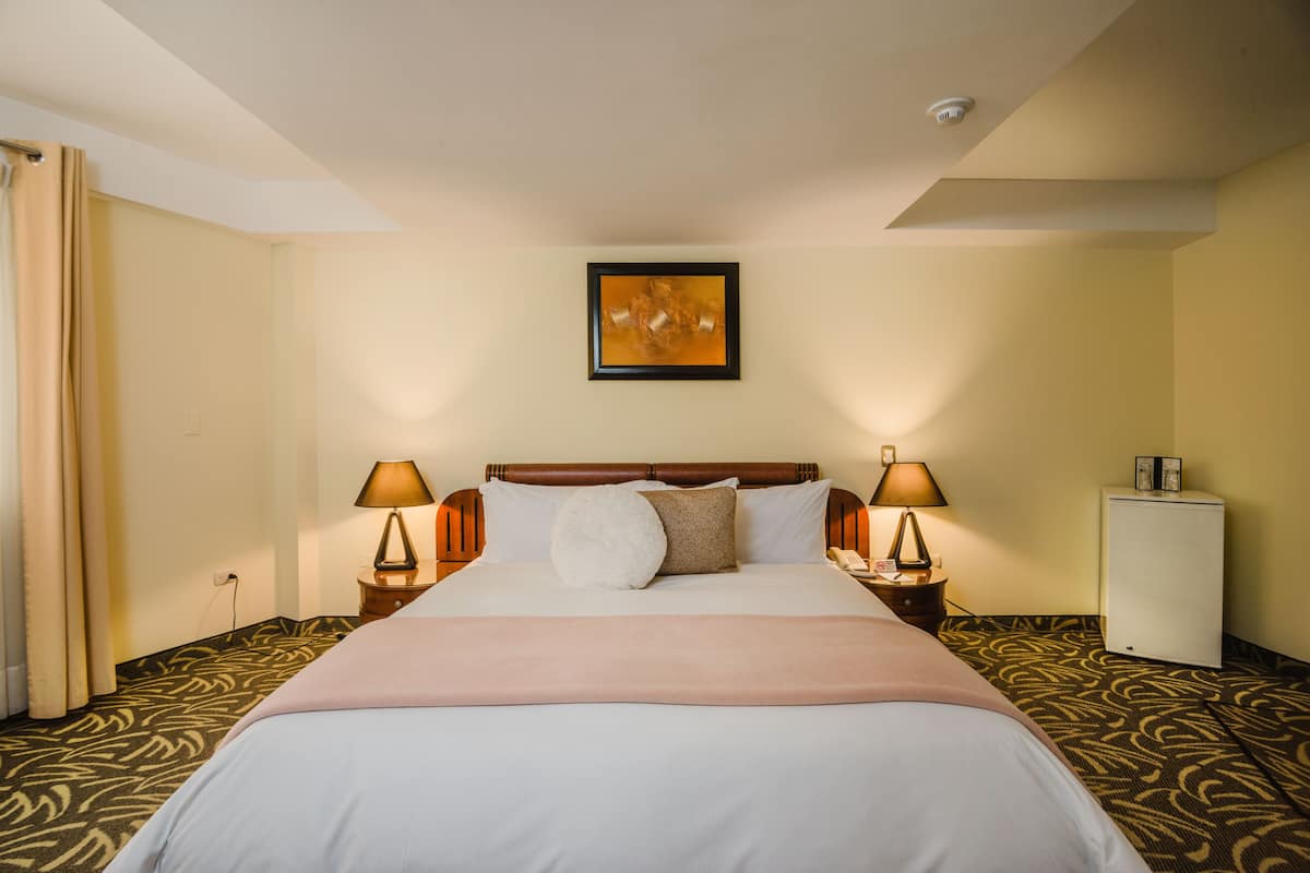A hotel room with a bed, two bedside tables with lamps, a wall-mounted picture, and a small white cabinet.
