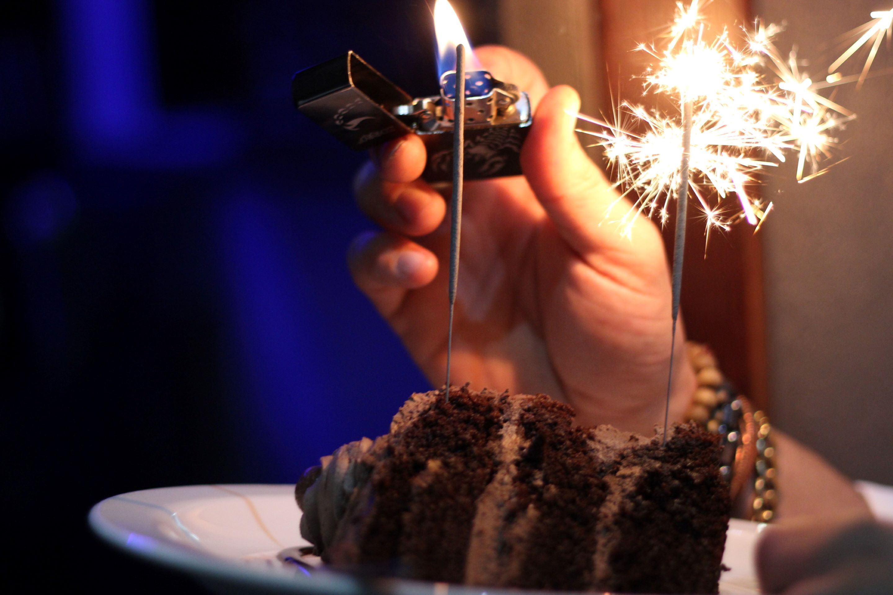 A hand holding a lighter with a lit sparkler over a cake.