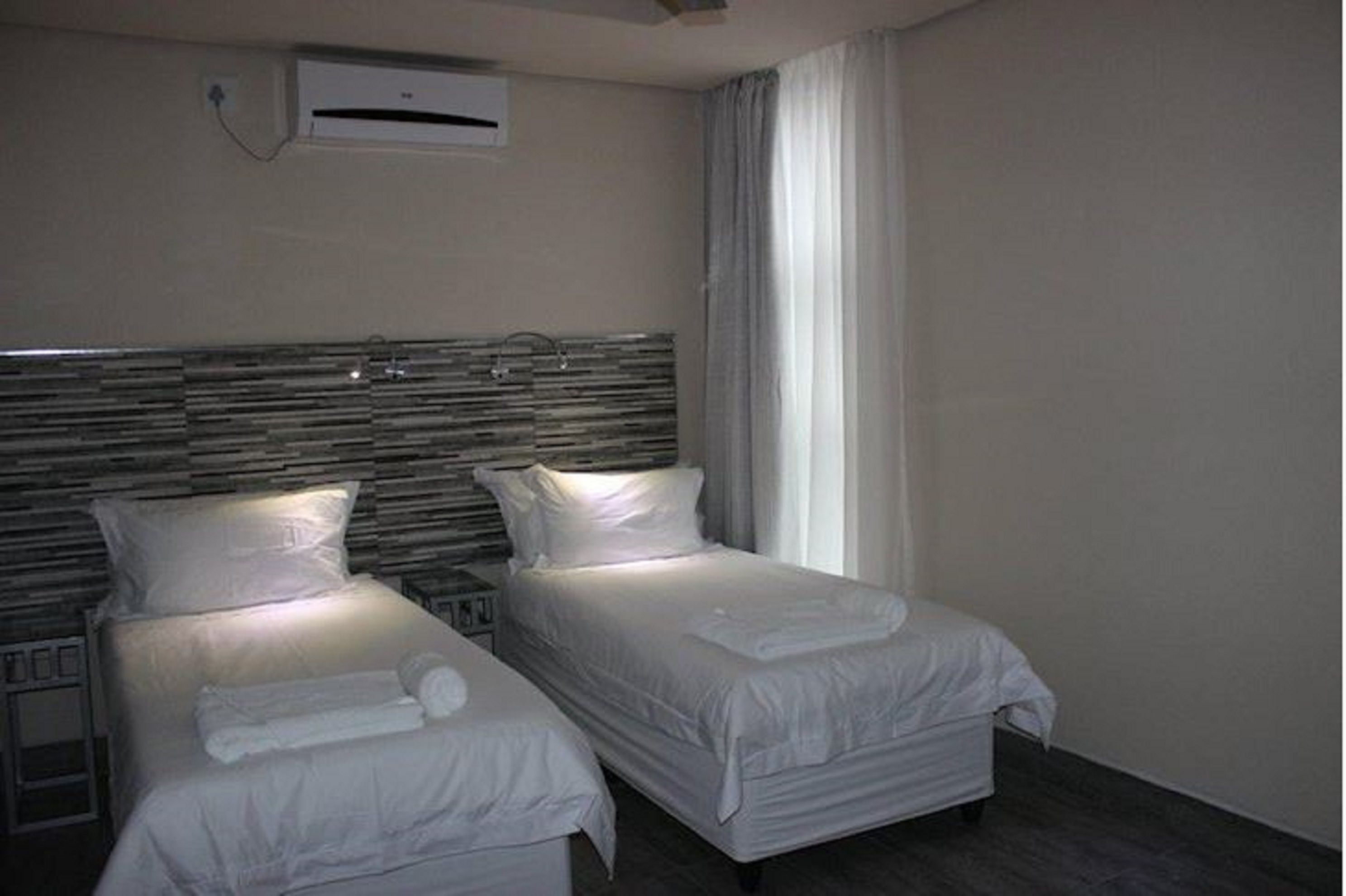 Habitación de hotel con dos camas, un cabecero moderno, un aire acondicionado de pared y un ventanal con cortinas.