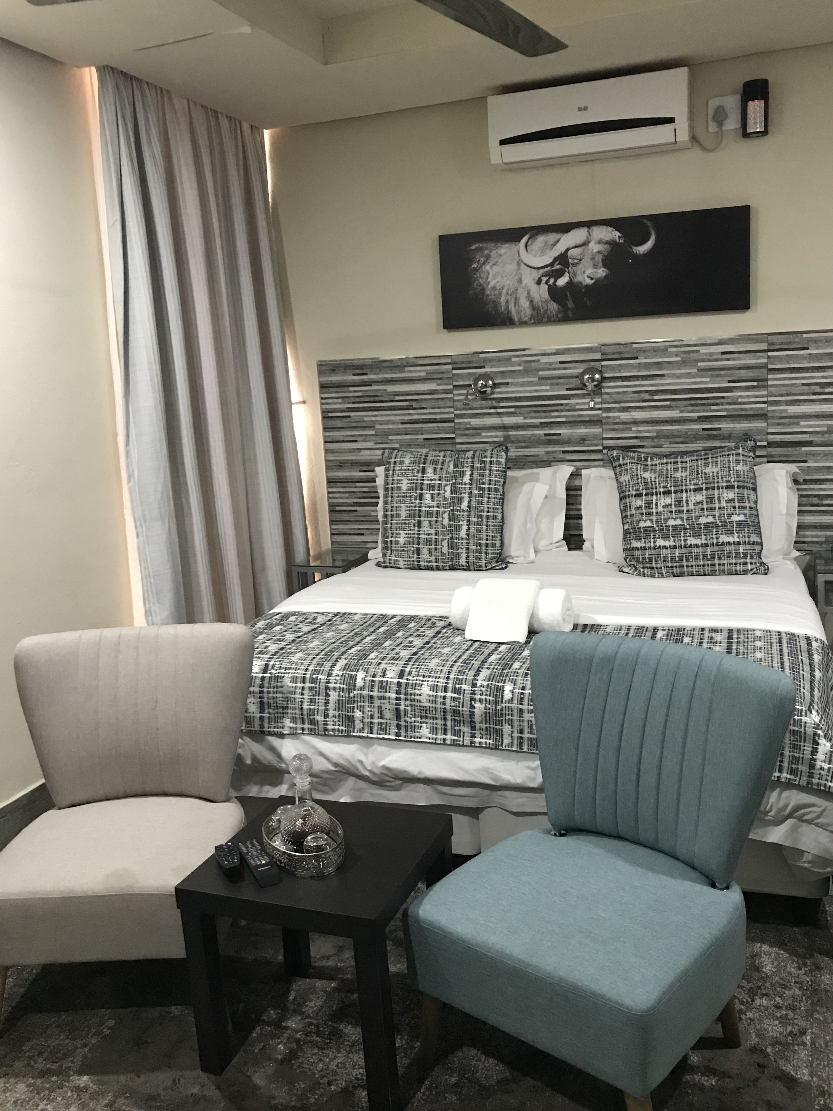 Ett hotellrum med en säng, två stolar, ett litet bord, en luftkonditionering och en tavla på väggen.