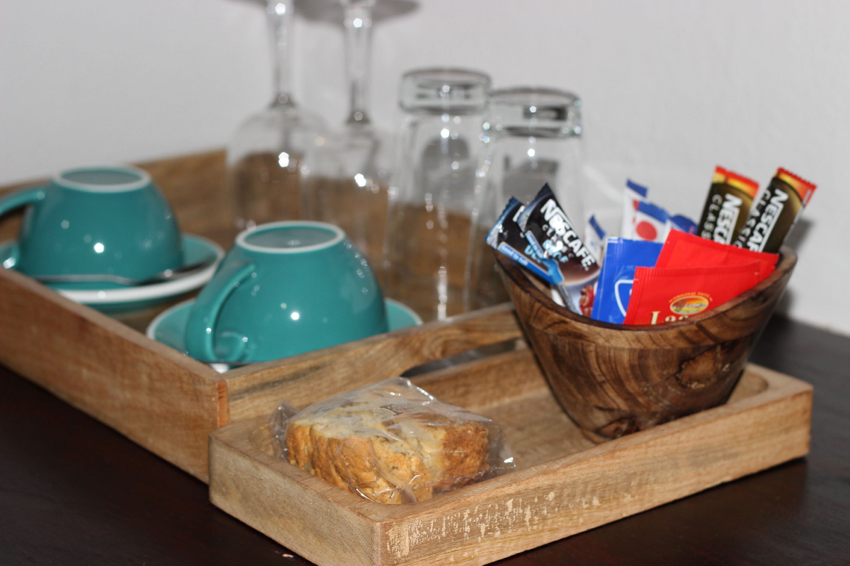Una bandeja de madera con un vaso de jugo, un pastel envuelto y un bol con diversas botanas empaquetadas.