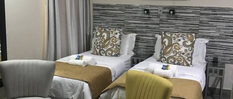 A hotel room with two beds, a chair, a small table, an air conditioning unit, and a ceiling fan.