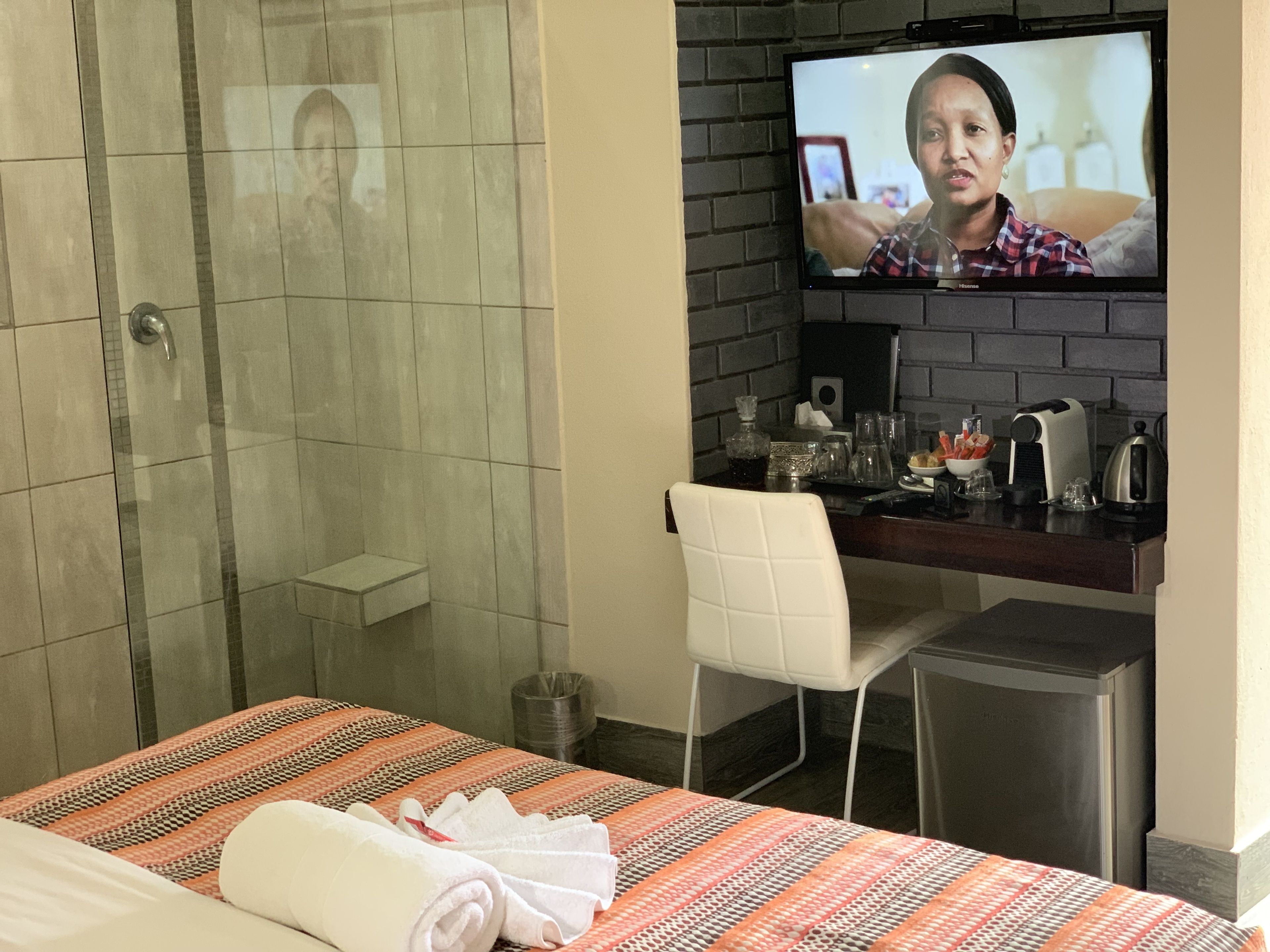 A hotel room with a bed, a shower, a desk with a TV, and a chair.