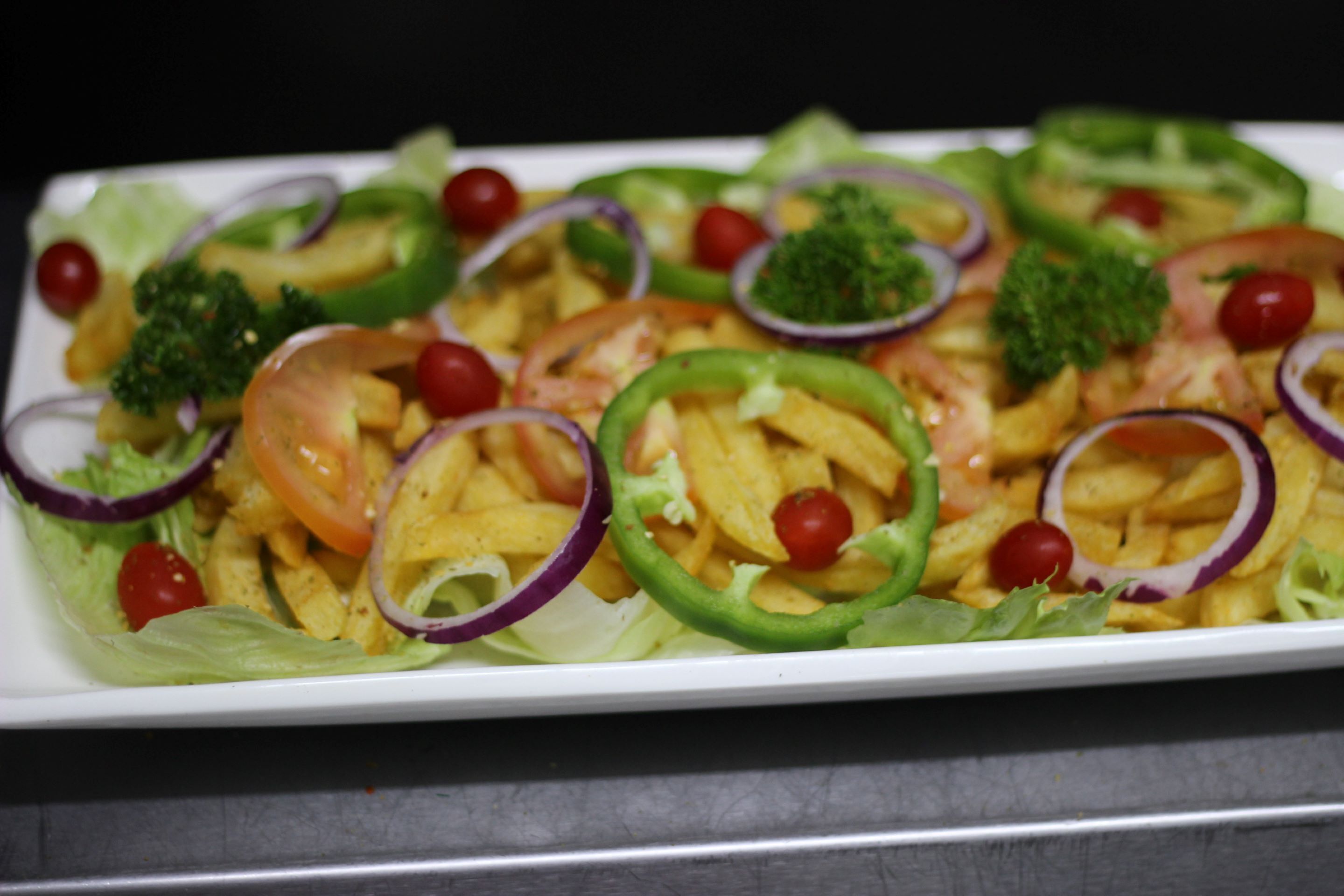Un piatto bianco rettangolare con un'insalata di lattuga, pomodori, cipolle rosse, peperoni verdi e broccoli.