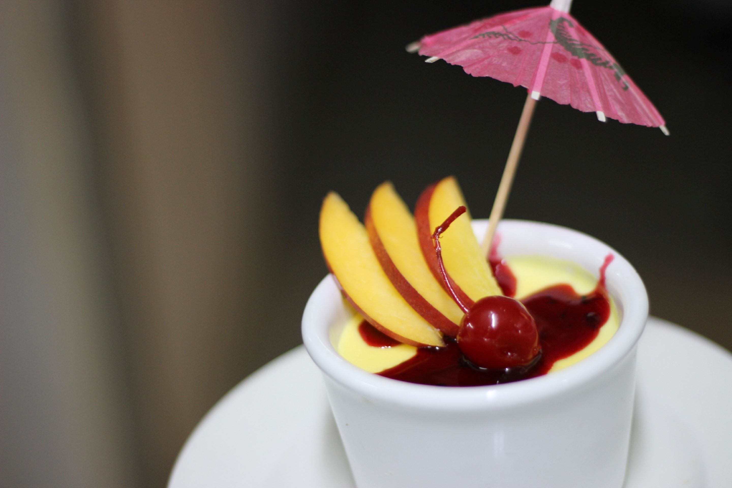 A dessert with sliced fruit and a cherry on top, served in a white bowl.