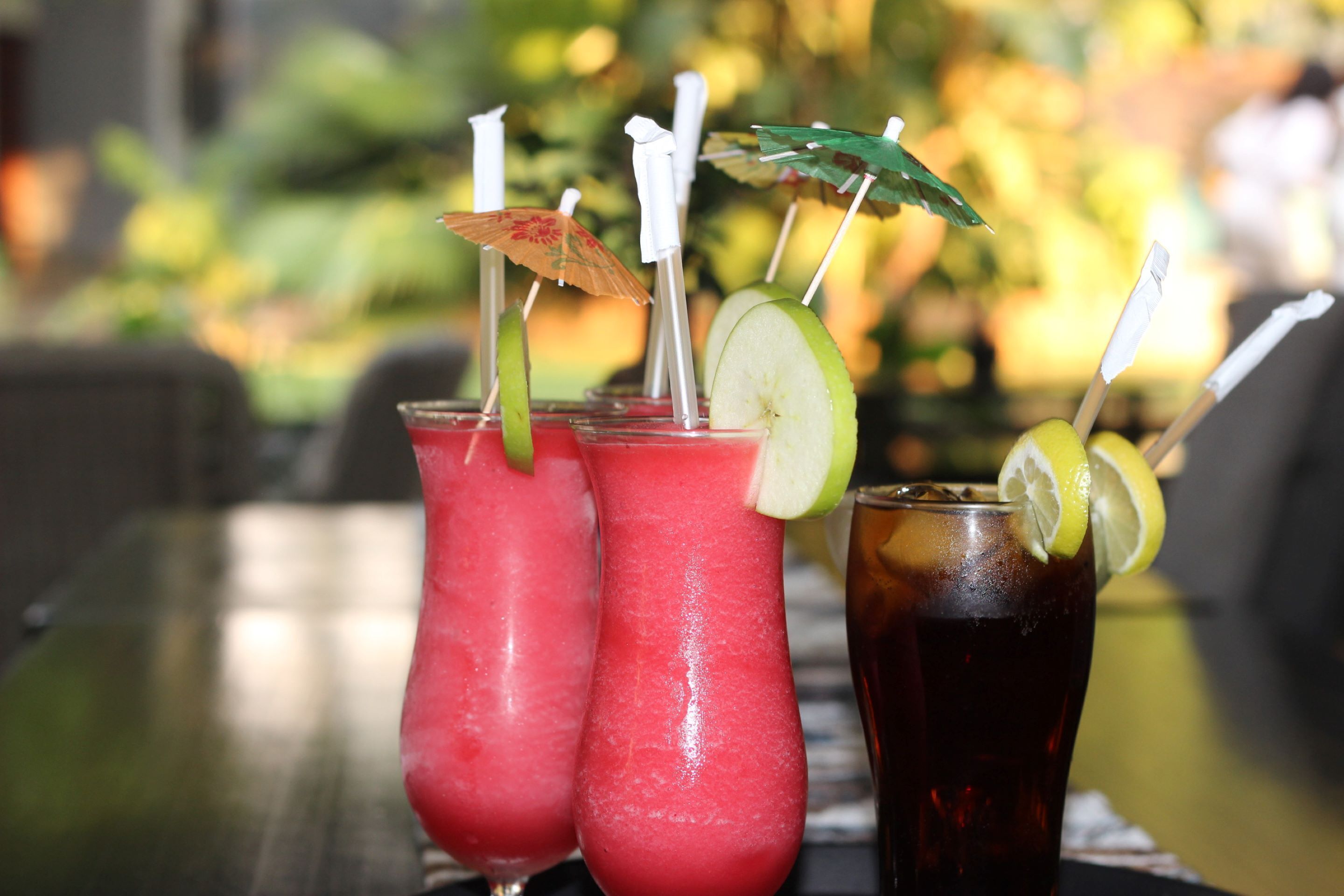 Three drinks on a table with a blurred outdoor background.