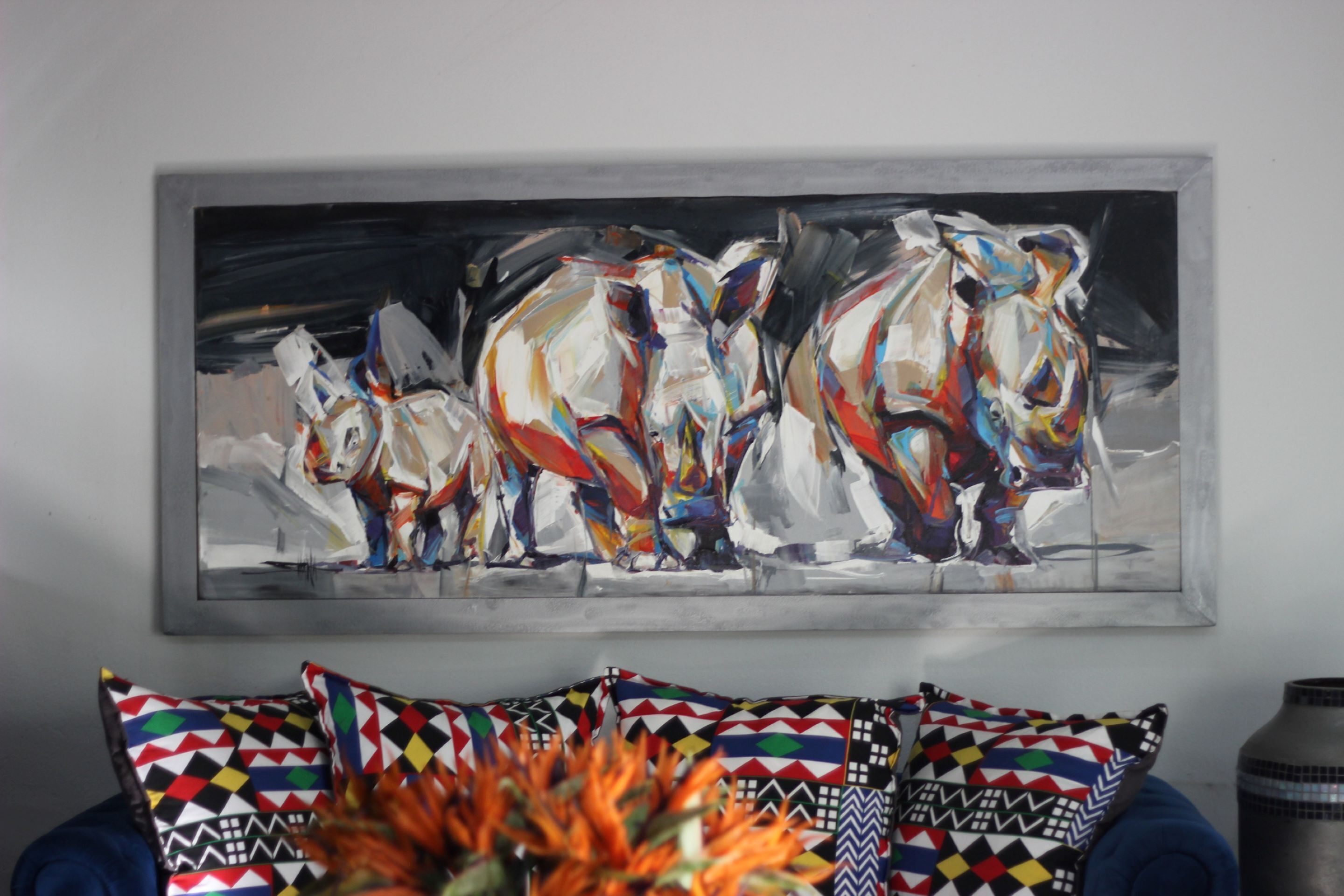 Una sala de estar moderna con un cuadro abstracto grande en la pared, cojines estampados coloridos y un jarrón con flores naranjas.