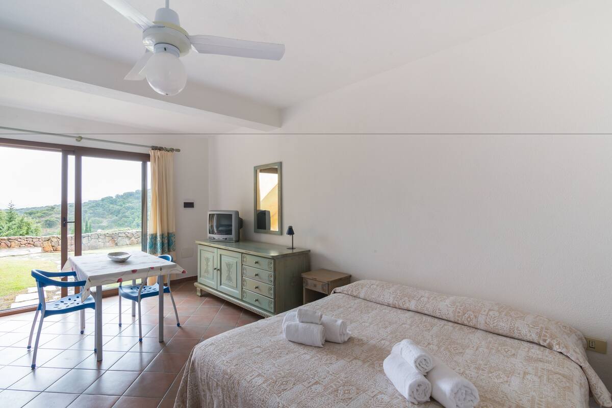 A bedroom with a bed, a desk with a chair, a television, and a dresser.