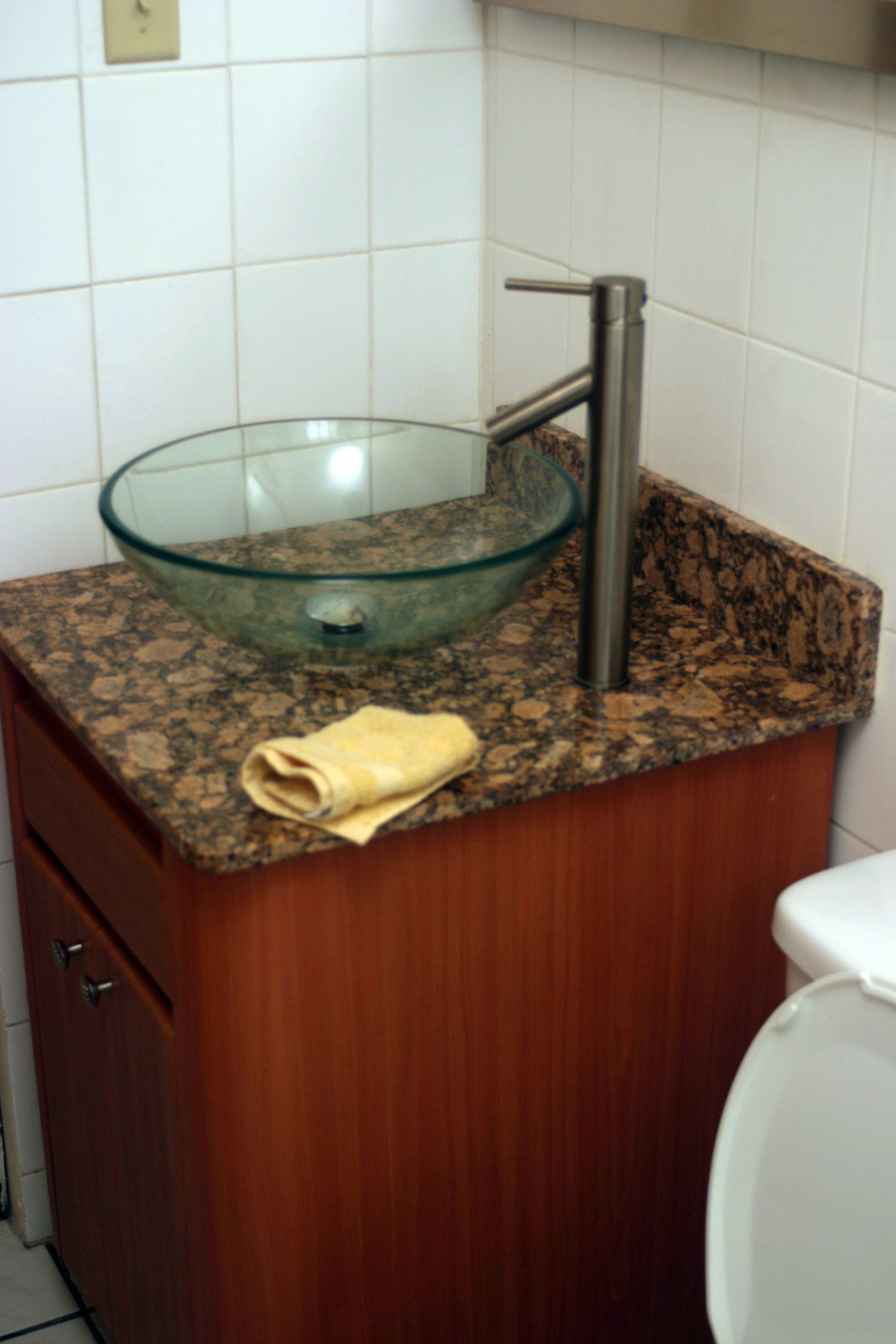 Un baño con lavamanos de vidrio, tocador de madera y un inodoro blanco.