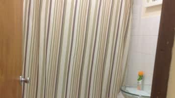 A bathroom with a striped shower curtain, a toilet, a glass sink, and a blue trash bin.