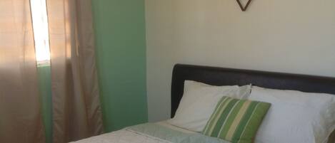 A neatly made bed with a quilted white cover, a green and white striped pillow, and a decorative wall piece above it.