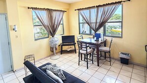 A living room with a sofa, a dining table with chairs, a TV, and a fan.