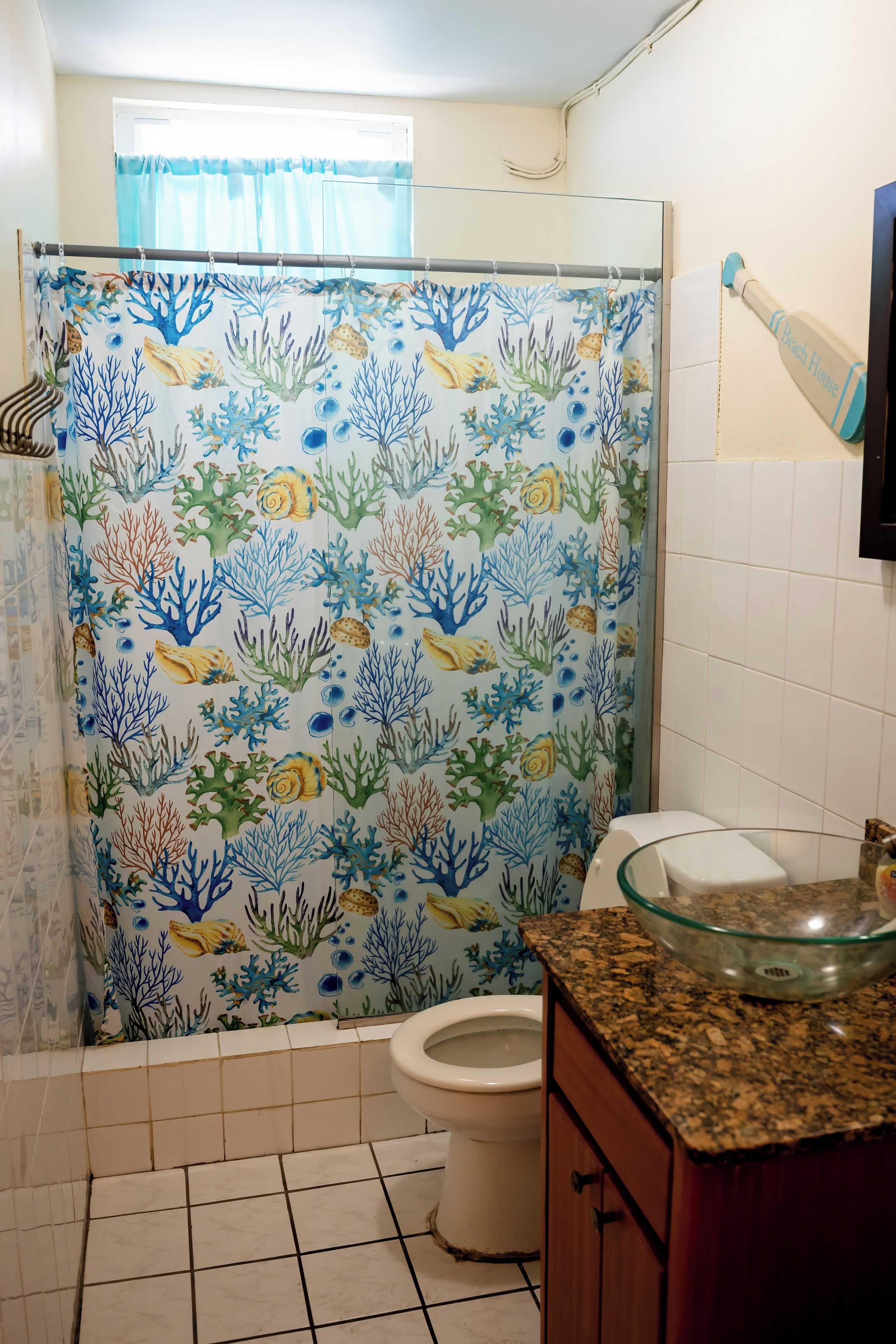 A bathroom with a shower curtain featuring an underwater theme, a toilet, and a glass bowl sink.