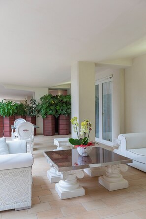 A modern living room with white furniture, a glass coffee table, and large windows. - Paradiso Hotel Bovelacci (Cervia)