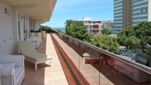 A balcony with sun loungers and a glass railing overlooking a coastal area with buildings and trees. - Paradiso Hotel Bovelacci (Cervia)