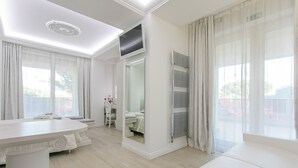 A modern, well-lit room with a large white table, a sofa, and a mirror reflecting a bathroom. - Paradiso Hotel Bovelacci (Cervia)