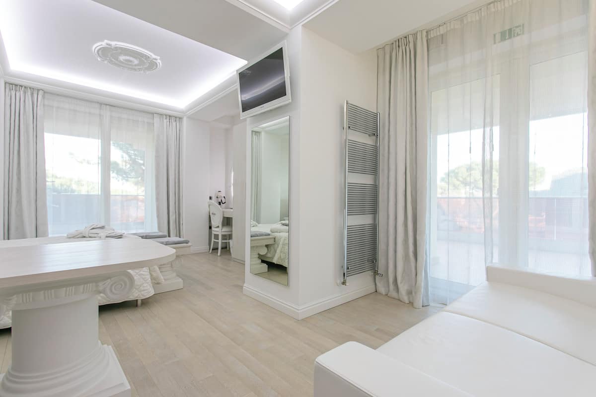 A modern, well-lit room with a large white table, a sofa, and a mirror reflecting a bathroom.