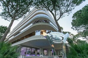 A multi-story hotel with a curved facade, a prominent sign for the Paradiso Hotel, and lush greenery surrounding the building. - Paradiso Hotel Bovelacci (Cervia)