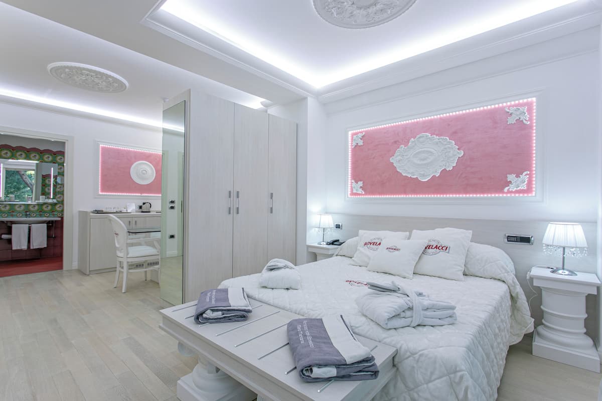 A modern hotel room with a large bed, bedside tables, a desk, and a vanity with a mirror.
