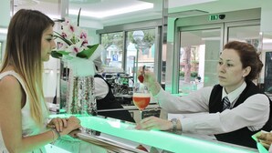 A bar area with a counter, a person holding a drink, and a flower arrangement. - Paradiso Hotel Bovelacci (Cervia)