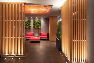Una moderna zona de recepción con un conjunto de asientos rojos, paneles de madera y un techo con iluminación natural.