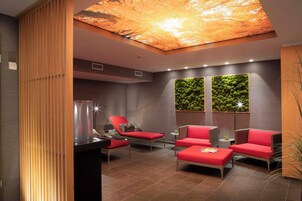 Un área de descanso moderna con una lámpara de techo, una planta verde en la pared y asientos rojos.