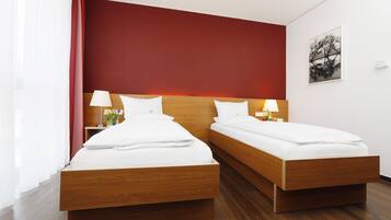 A hotel room with two wooden beds, white bedding, and a red accent wall.