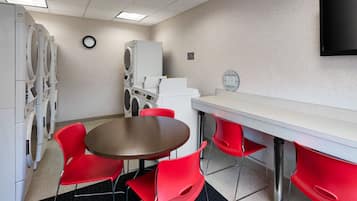 Una habitación con una mesa redonda y cuatro sillas rojas, un mostrador blanco y una lavadora.