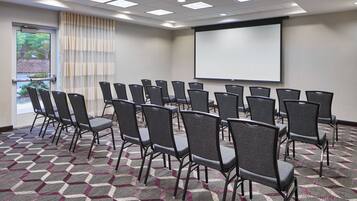 A conference room with rows of chairs, a projector screen, and a patterned carpet.