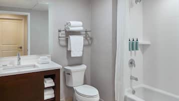Uma casa de banho com sanita, lavatório e banheira. Existem toalhas e produtos de higiene pessoal nas prateleiras.
