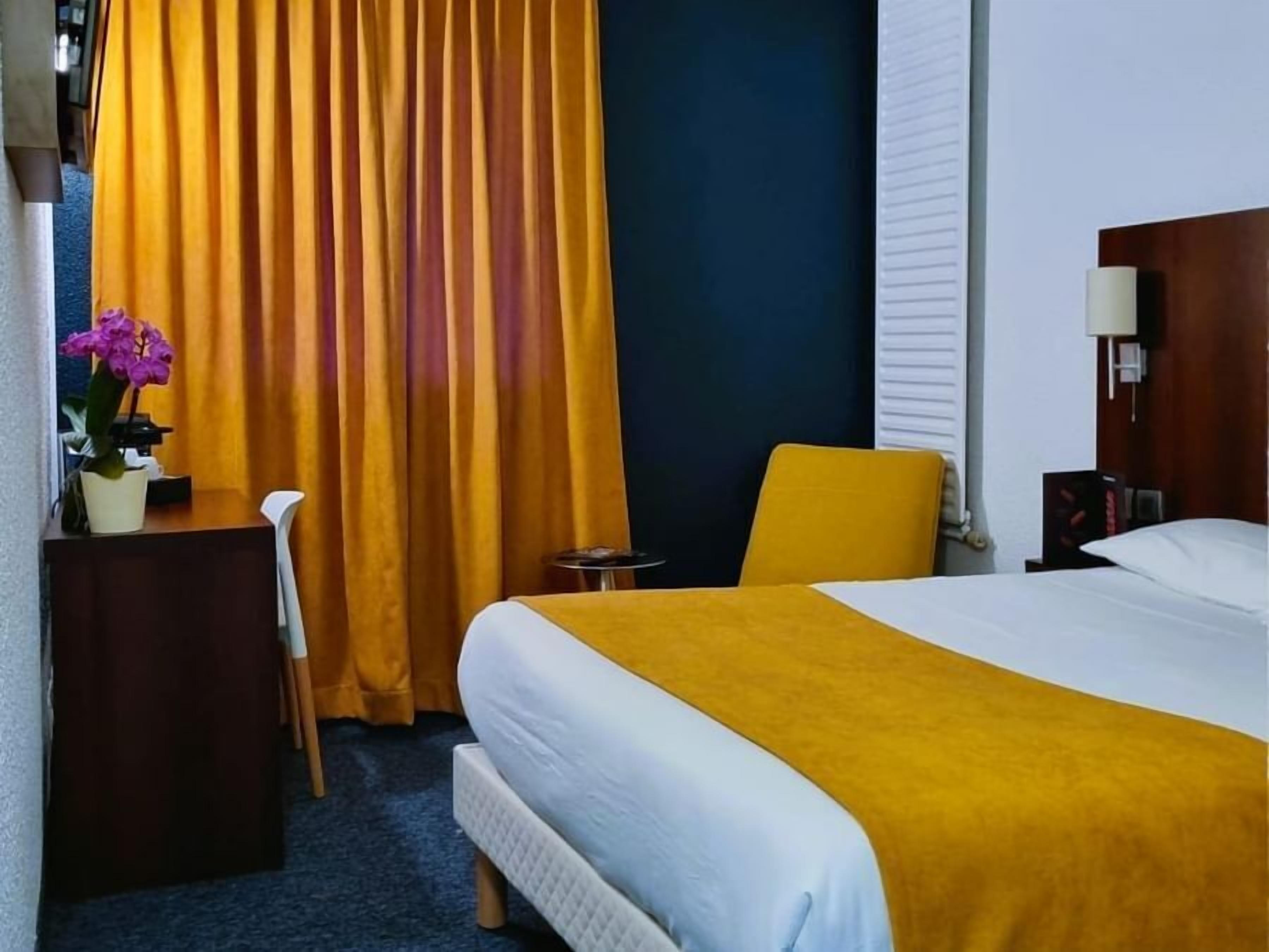 A hotel room with a bed, a desk, a chair, a small table, and a curtain.