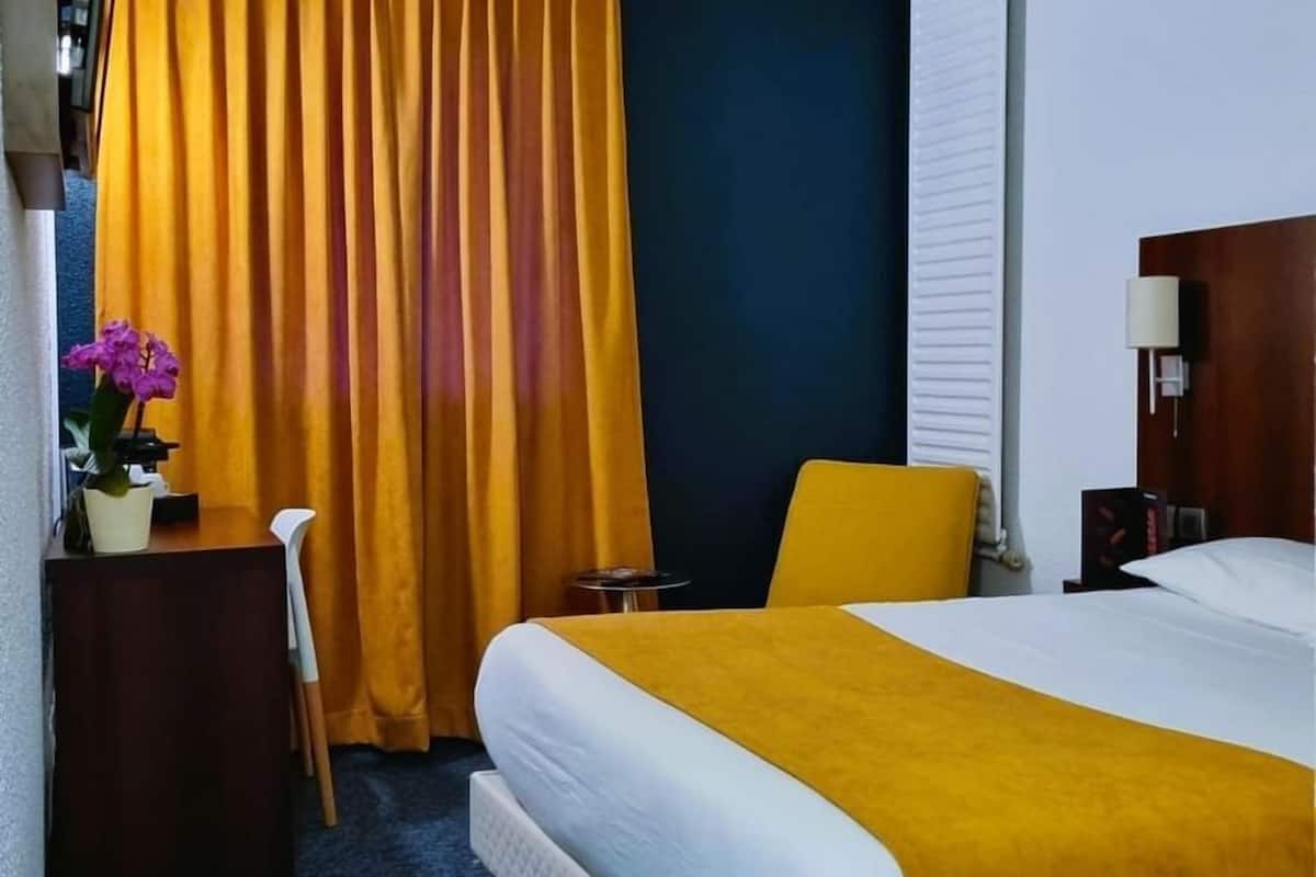 Une chambre d’hôtel avec un lit, un bureau, une chaise, une petite table et un rideau.