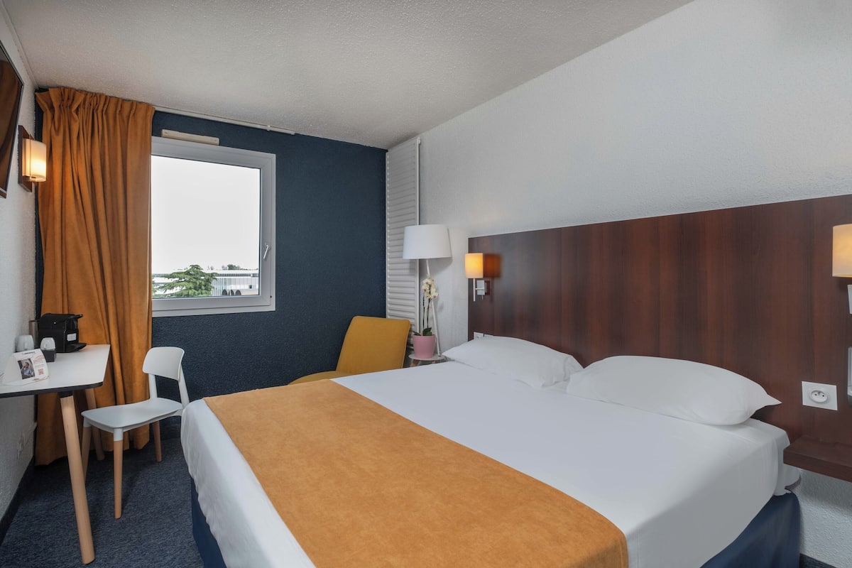 A hotel room with a bed, a desk, a chair, and a window with curtains.
