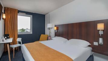Una habitación de hotel con cama, escritorio, silla y ventana con cortinas.