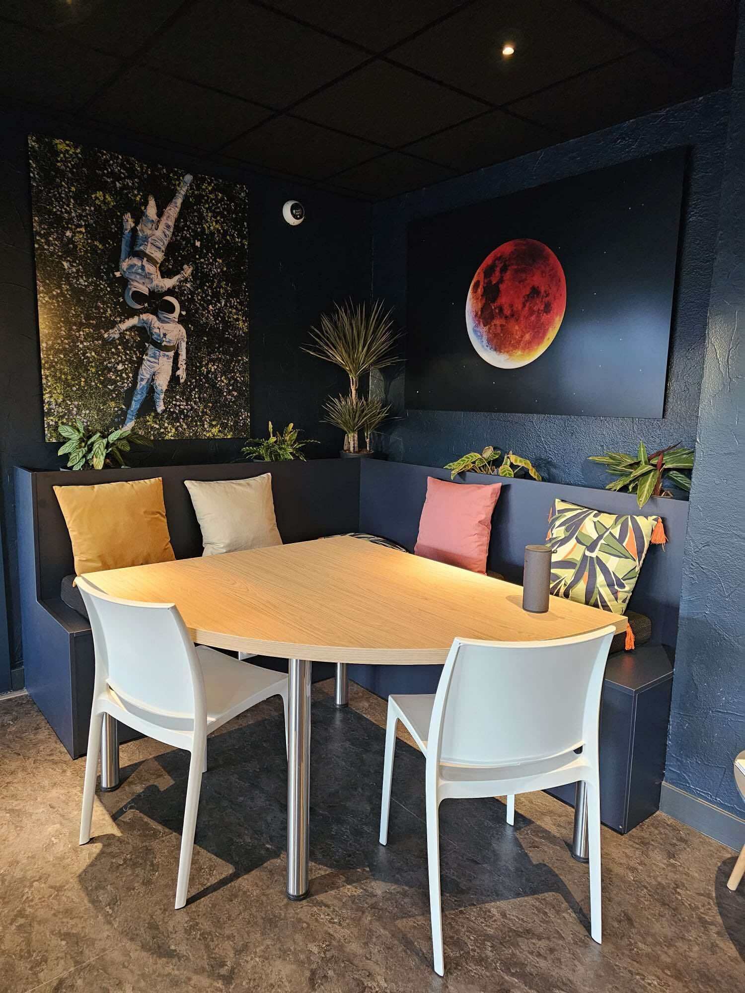 A modern dining area with a round table, white chairs, and a dark blue accent wall with a large painting of a red moon.