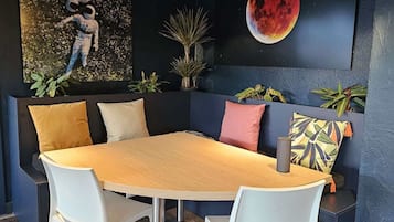 A modern dining area with a round table, white chairs, and a dark blue accent wall with a large painting of a red moon.