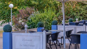 An outdoor seating area with tables and chairs, surrounded by greenery and a decorative fence. - The originals Hotel Ariane, Toulouse (Toulouse)