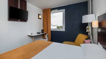 Een hotelkamer met een bed, bureau, televisie, raam met gordijnen en een lamp.