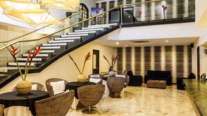 A modern hotel lobby with a staircase, wicker furniture, and a glass railing. - Hotel Ciudad Bonita (Bucaramanga)