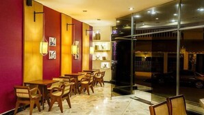 A restaurant with wooden tables and chairs, a red and yellow color scheme, and a view of the street through the glass wall. - Hotel Ciudad Bonita (Bucaramanga)