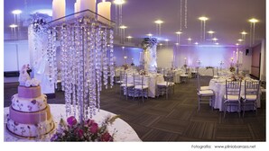 A wedding reception hall with round tables, chairs, and a tiered wedding cake. - Hotel Ciudad Bonita (Bucaramanga)