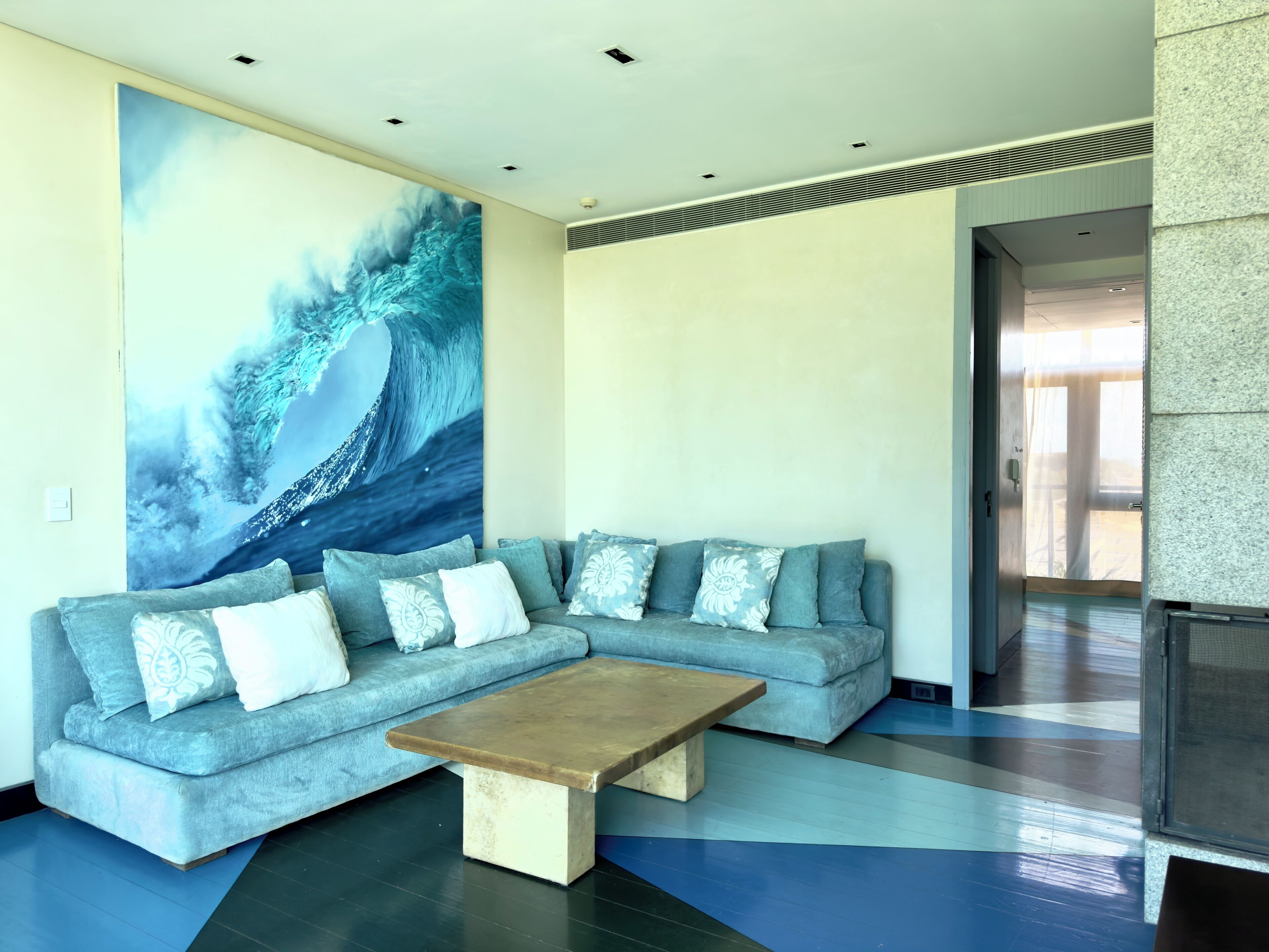 A modern living room with a grey sectional sofa, a wooden coffee table, and a large abstract painting on the wall.