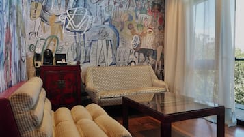 Una sala de estar con un sofá estampado, un aparador rojo y una mesa de centro de vidrio.