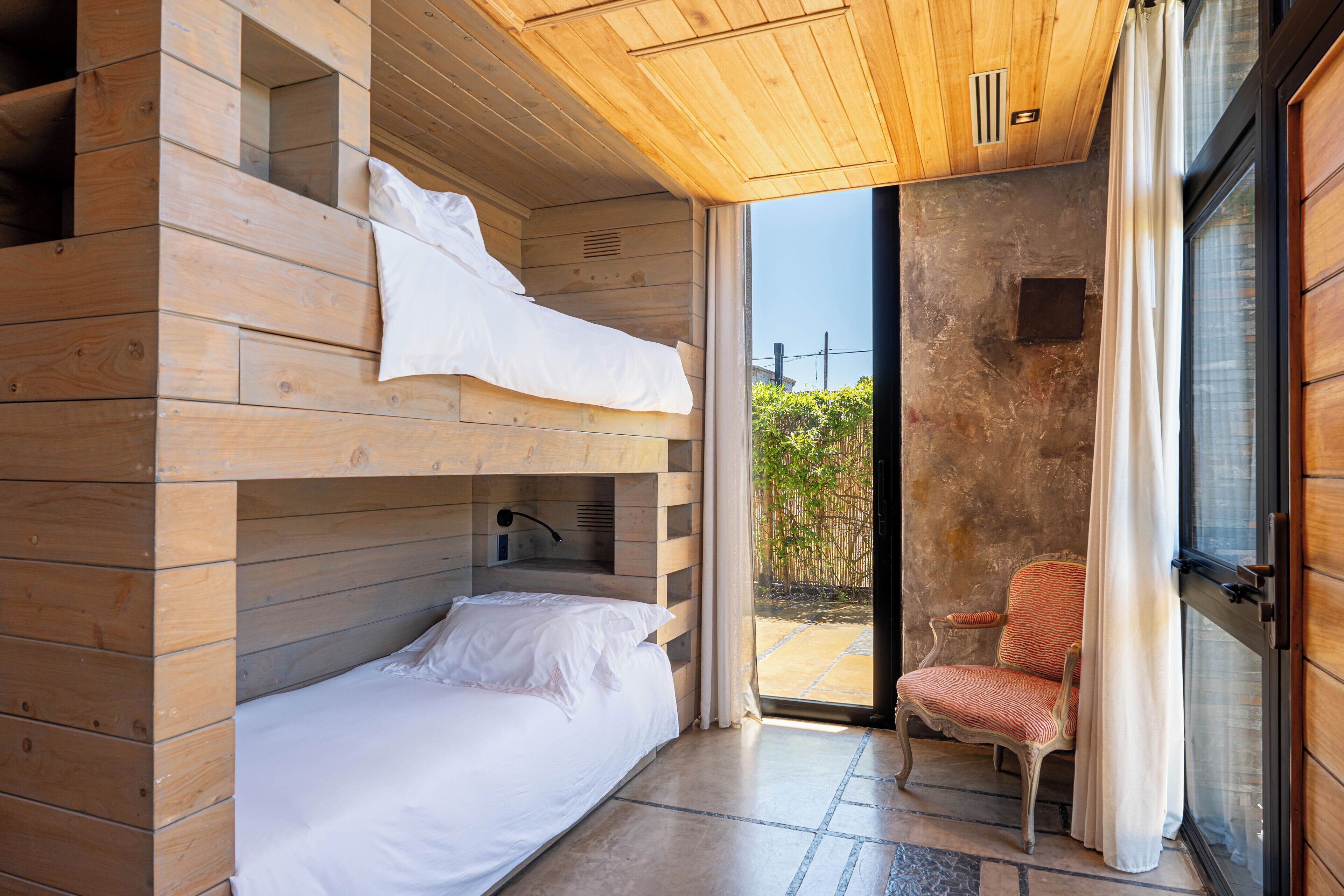 A wooden cabin room with a bunk bed, a chair, and a sliding glass door leading to an outdoor area.