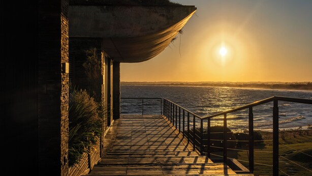 A wooden deck with a railing, overlooking a body of water at sunset. - Playa Vik Jose Ignacio (José Ignacio)