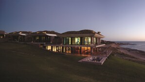 A modern coastal house with a large glass facade, a spacious outdoor seating area, and a view of the ocean. - Playa Vik Jose Ignacio (José Ignacio)